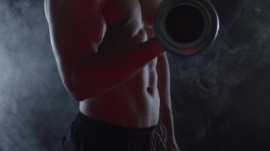 Dumanlı genç ve formda bir adamın silueti dambılla biseptik kıvrımlar yapıyor. Yavaş çekim, dikey döndürme