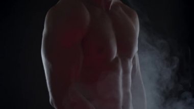 Bisepslerini gösteren dumandaki genç ve zinde bir adamın silueti. Yavaş çekim, dikey döndürme