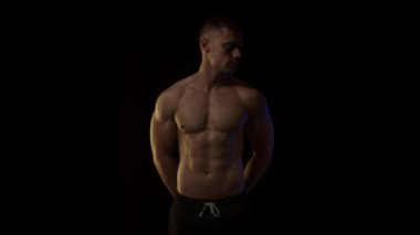 Siyah arka plandaki genç fit adam. Yavaşça yakınlaştır. Sanatsal renkli ışık