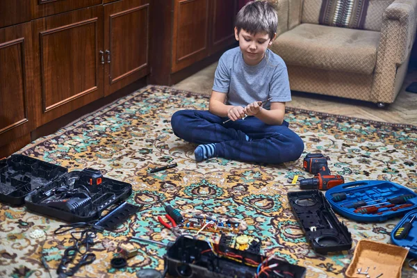 A boy, eight years old, disassembles an old radio, sitting on the carpet in the apartment