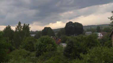 Yeşil ağaçlarla çevrili küçük bir köyün üzerinde fırtına bulutları asılı.