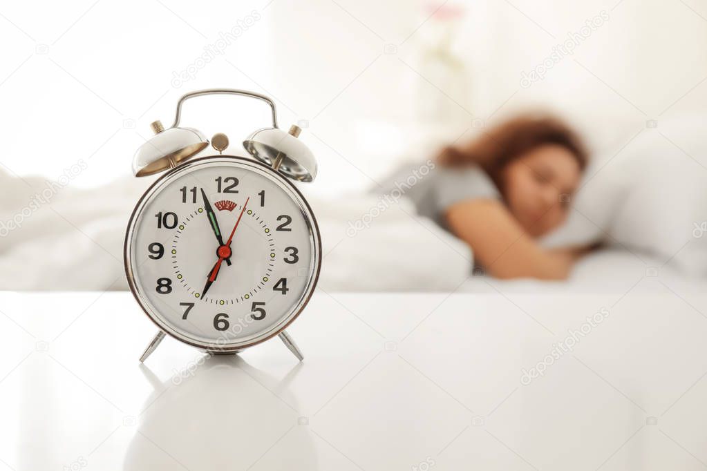 Alarm clock on table in bedroom of beautiful young woman. Morning time