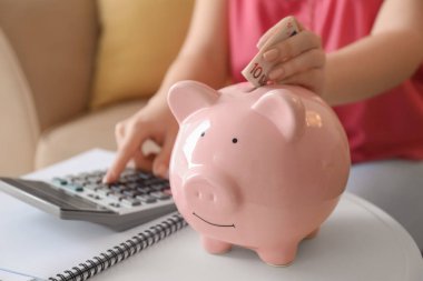 Hesap makinesinde sayma ve euro banknot kumbara kapalı, closeup koyarak genç kadın. Para tasarruf kavramı