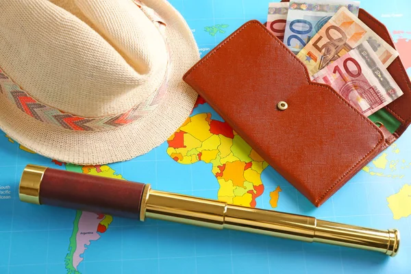 Spyglass, hat and wallet with money on world map. Travel planning concept