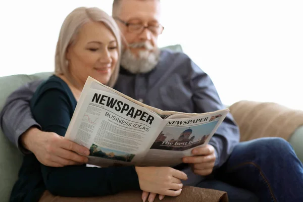 Mature couple reading newspaper at home