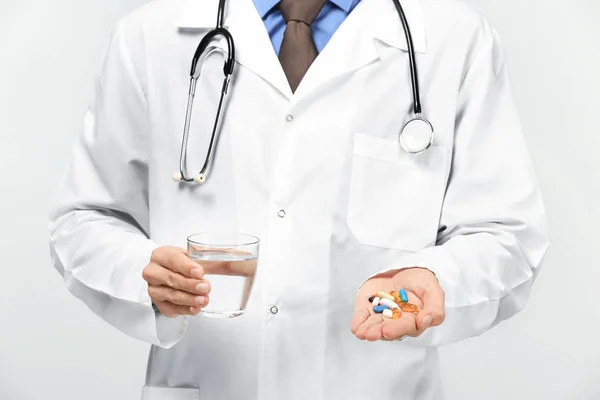 白い背景の上の丸薬が付いている水のガラスを保持している男性医師 — ストック写真