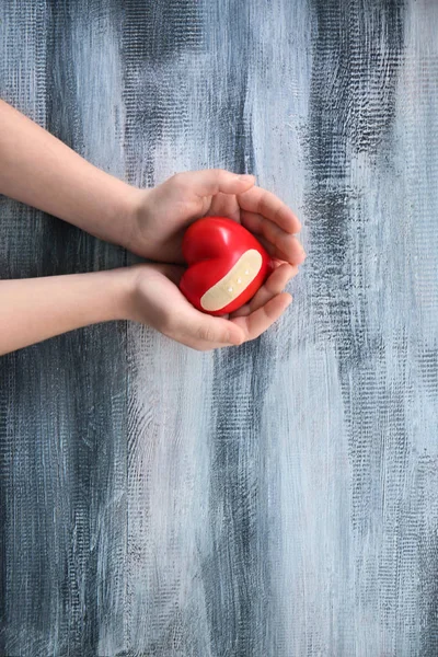 Child holding red heart with medical plaster on wooden background.  Health care concept