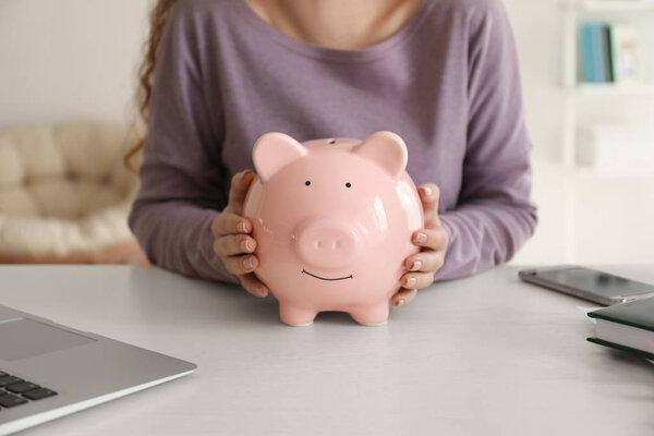 Young woman holding piggy bank indoors, closeup. Money savings concept