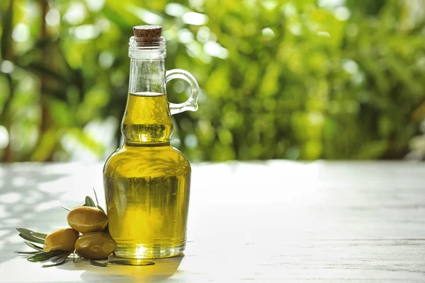 Glass jug with fresh oil and canned olives on table outdoors