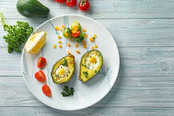 Baked avocado with eggs and vegetables on white wooden background