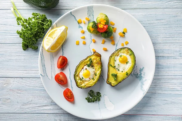 Baked avocado with eggs and vegetables on white wooden background