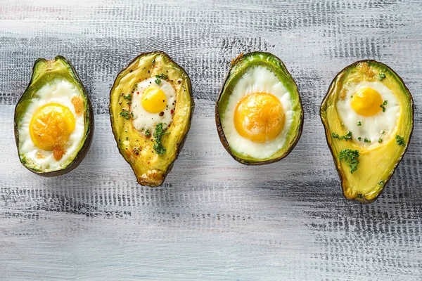 Baked avocados with eggs and vegetables on wooden table