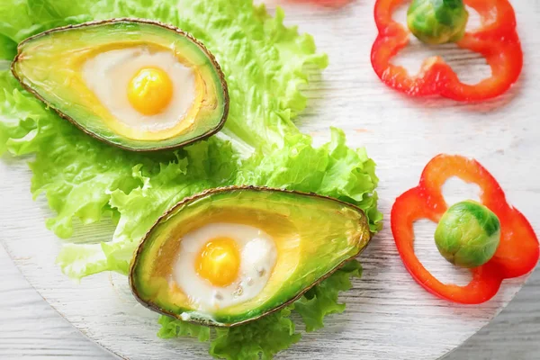 Baked avocado with eggs and vegetables on wooden board, closeup