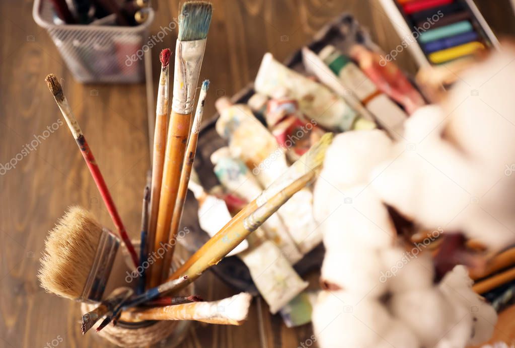 Holder with brushes on table and paints in artist's workshop