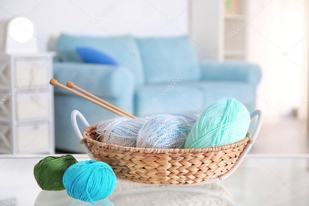 Wicker basket with knitting yarn and needles on glass table