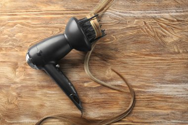Diffuser hair dryer with strand of blonde hair on wooden background clipart