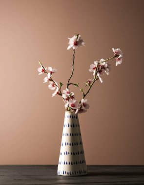 Masanın üzerinde renk arkaplanına karşı çiçek açan güzel dalları olan vazo