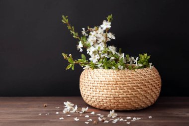 Ahşap masa üzerinde çiçek dalları ile hasır kutu