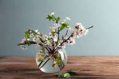 Ahşap masanın üzerinde çiçek açan güzel dalları olan bir vazo.