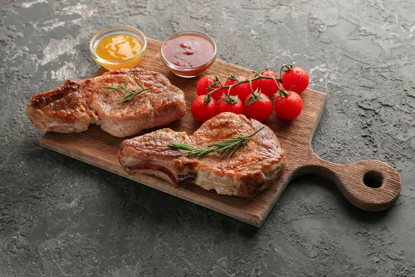 Wooden board with tasty grilled steak, tomatoes and sauces on table
