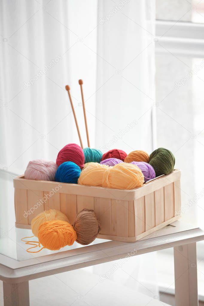 Box with colorful knitting yarns and needles on table indoors