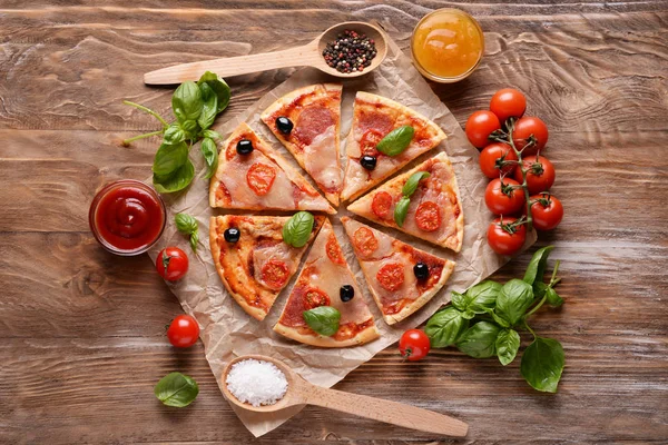 Pieces of tasty pizza with sauces and spices on wooden background, flat lay