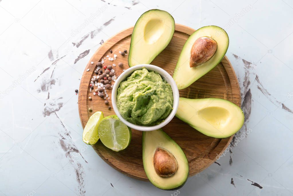 Bowl with delicious guacamole, spices and ripe avocados on wooden board