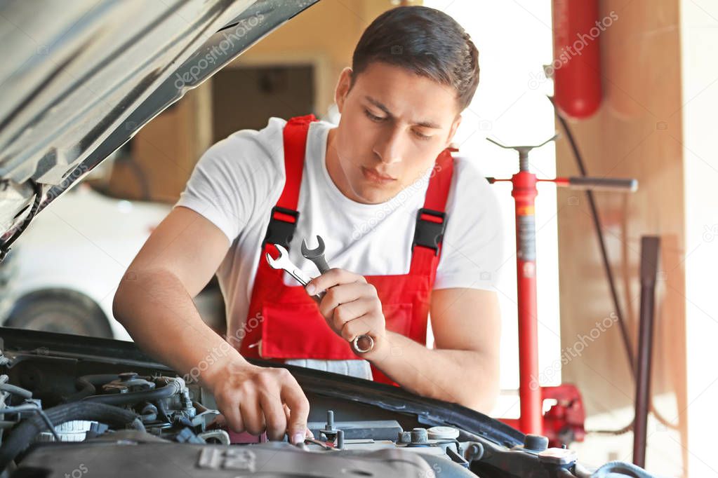 Young auto mechanic repairing car in service center