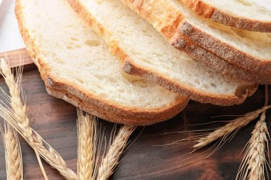 Taze ekmek ve buğday kulakları ahşap plaka üzerinde closeup dilimlenmiş