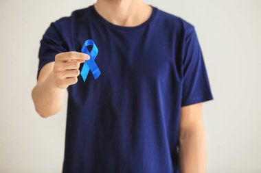 Man holding blue ribbon on light background. Prostate cancer concept clipart