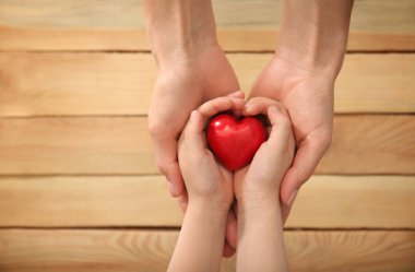 Anne ve çocuk ahşap arka plan üzerinde kırmızı kalp tutan eller