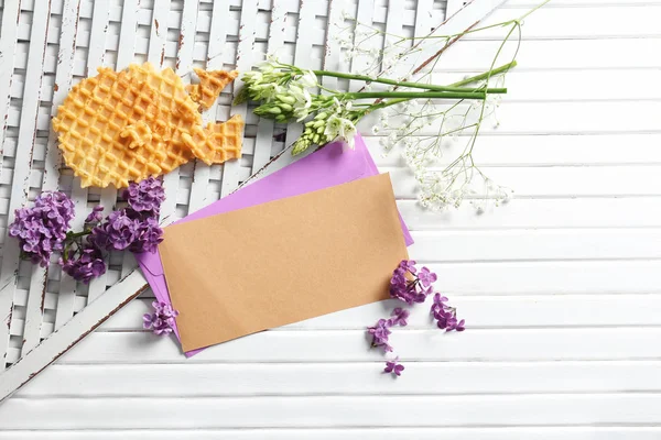 Mail envelopes with flowers and waffles on white wooden background