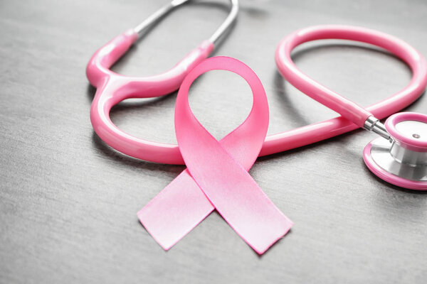 Pink ribbon and stethoscope on light background, closeup. Breast cancer awareness concept