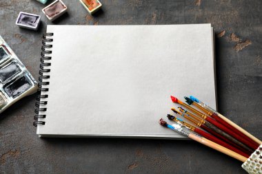 Notebook with paint brushes on grey background clipart