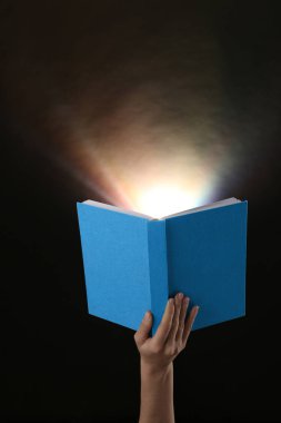 Koyu arka plan üzerinde parlayan ile el holding açık kitap