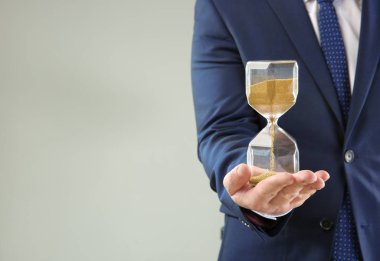 Gri arka plan üzerinde kum saati tutan adam. Zaman yönetimi kavramı