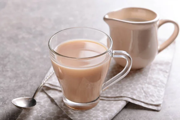 Glass cup of aromatic tea with milk on table