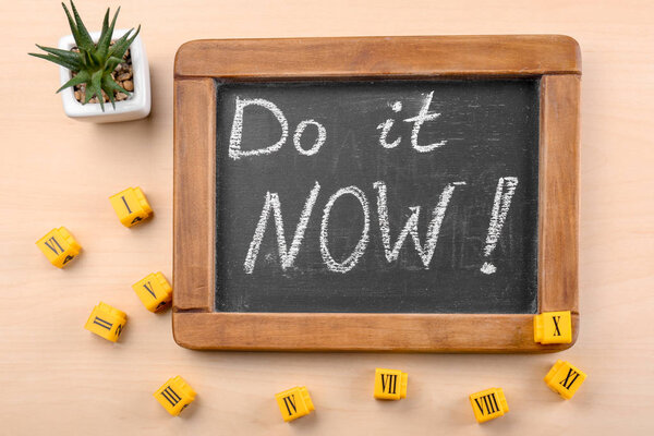 Chalkboard with phrase "Do it now" on table. Time management concept