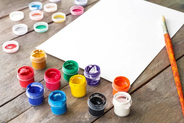 Paint jars with blank sheet of paper on wooden table