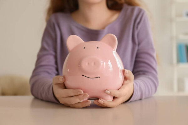 Young woman holding piggy bank indoors, closeup. Money savings concept