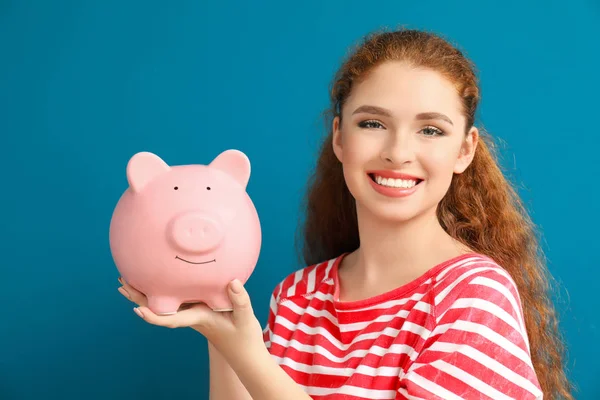年轻女子抱着小猪银行的颜色背景 货币储蓄概念 — 图库照片
