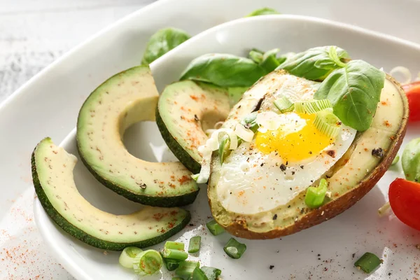 Tasty baked avocado with egg and fresh vegetables on plate, closeup