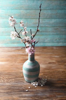 Ahşap masanın üzerinde çiçek açan güzel dalları olan bir vazo.
