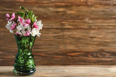 Ahşap masanın üzerinde çiçek açan güzel dalları olan bir vazo.