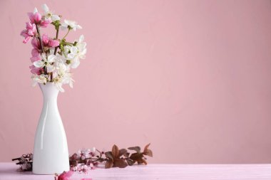 Masanın üzerinde renk arkaplanına karşı çiçek açan güzel dalları olan vazo