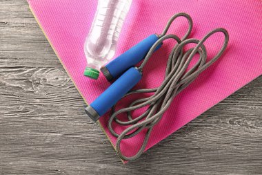 Yoga mat ile ip atlama ve şişe suyu ahşap arka plan üzerinde