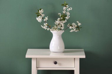 Masanın üzerinde renk arkaplanına karşı çiçek açan güzel dalları olan vazo