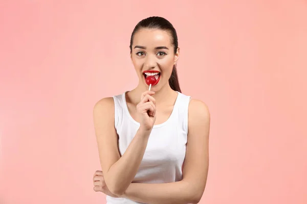 Attractive young woman with lollipop on color background