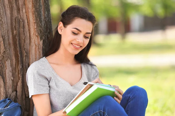 Beautiful young woman with notebook resting in park