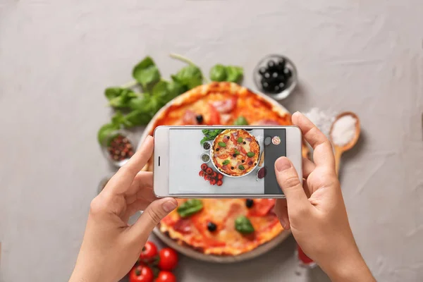 Woman taking photo of tasty pizza with mobile phone, top view